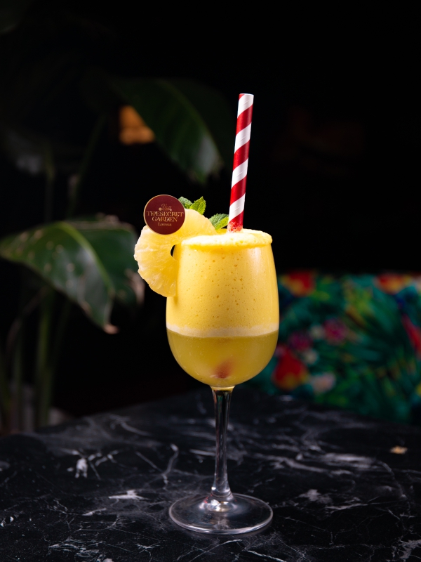 A Tall Yellow Tropical Cocktail Garnished With A Pineapple Wedge And A Red Striped Straw.